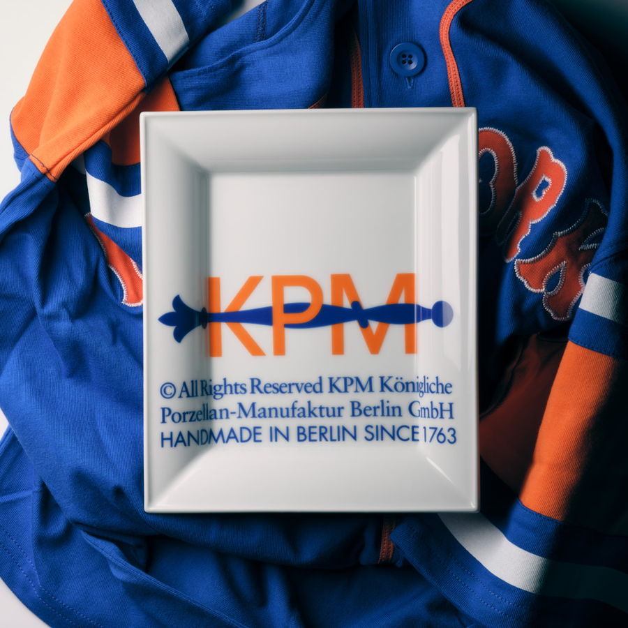KPM porcelain plate on a blue and orange sports jersey background.
