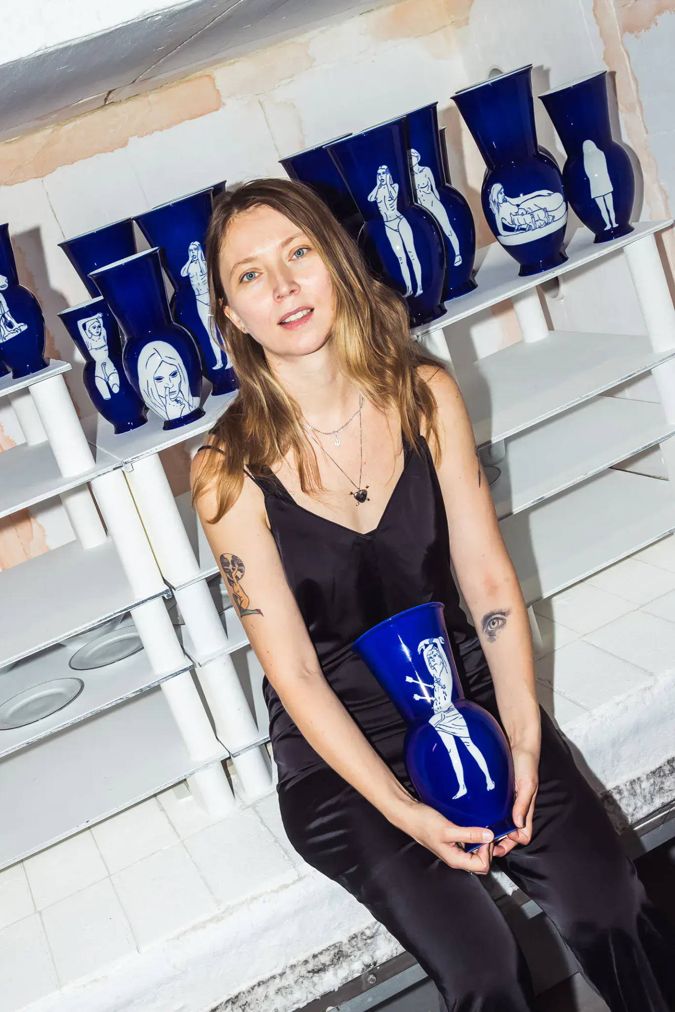 Julia Beliaeva in schwarzer Kleidung, die unter anderen Vasen eine blaue Vase in der Hand hält.