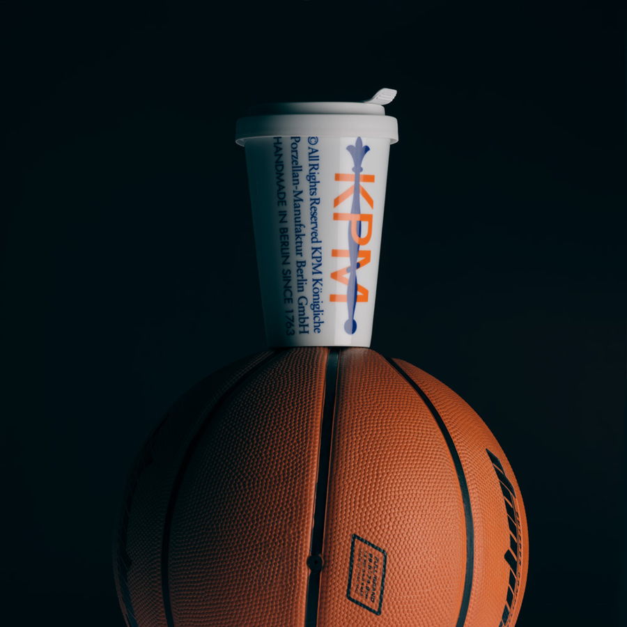 A basketball with a cup balanced on top against a dark background.