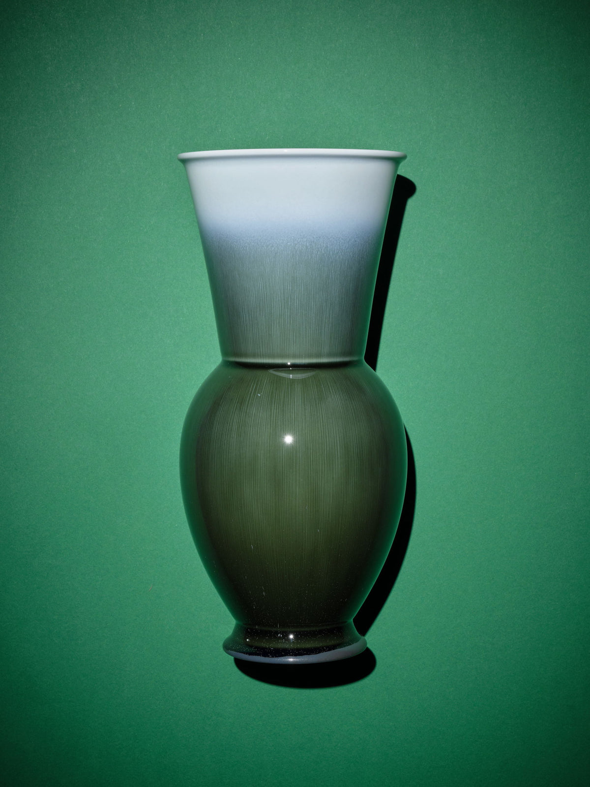 A green and white vase against a solid green background.