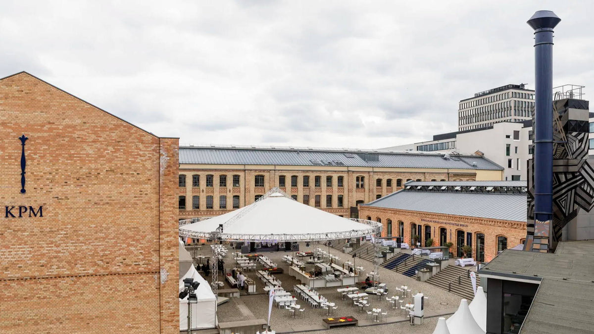 Urban courtyard with a large tent, surrounded by buildings and a cloudy sky.