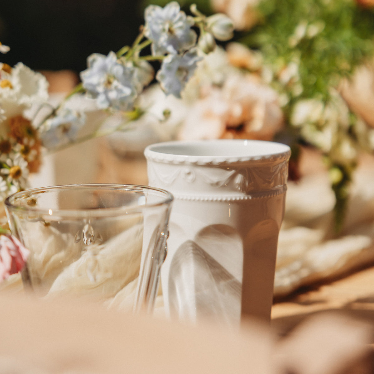 Un verre et une tasse blanche entourés de fleurs sur une table.