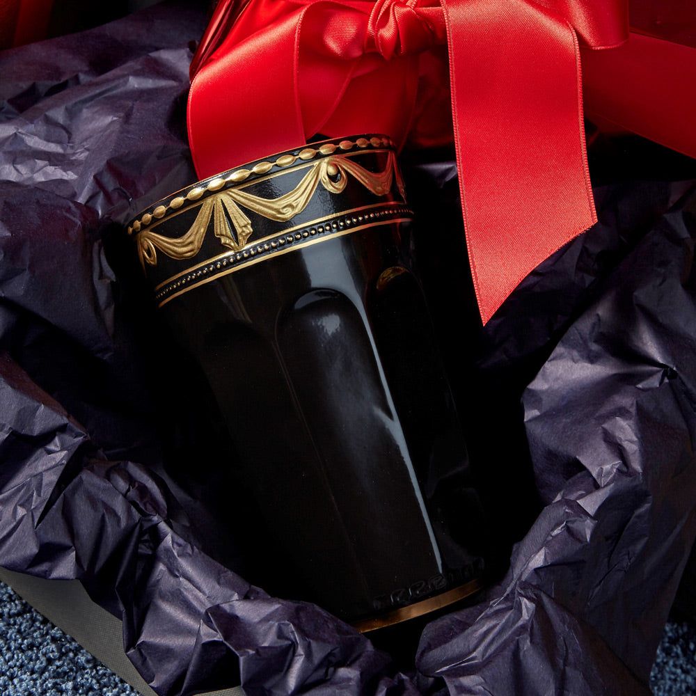 Une « Gobelets à champagne » KPM noire décorative, présentée dans un emballage cadeau orné d'un nœud rouge.