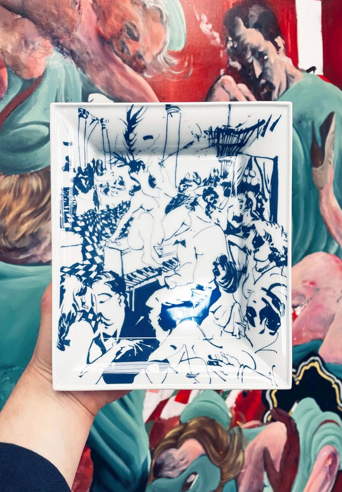 A hand holds a blue and white artwork against a colorful background.